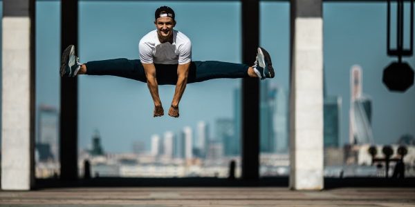 Man performing a split jump on concrete, showcasing fitness and agility.
