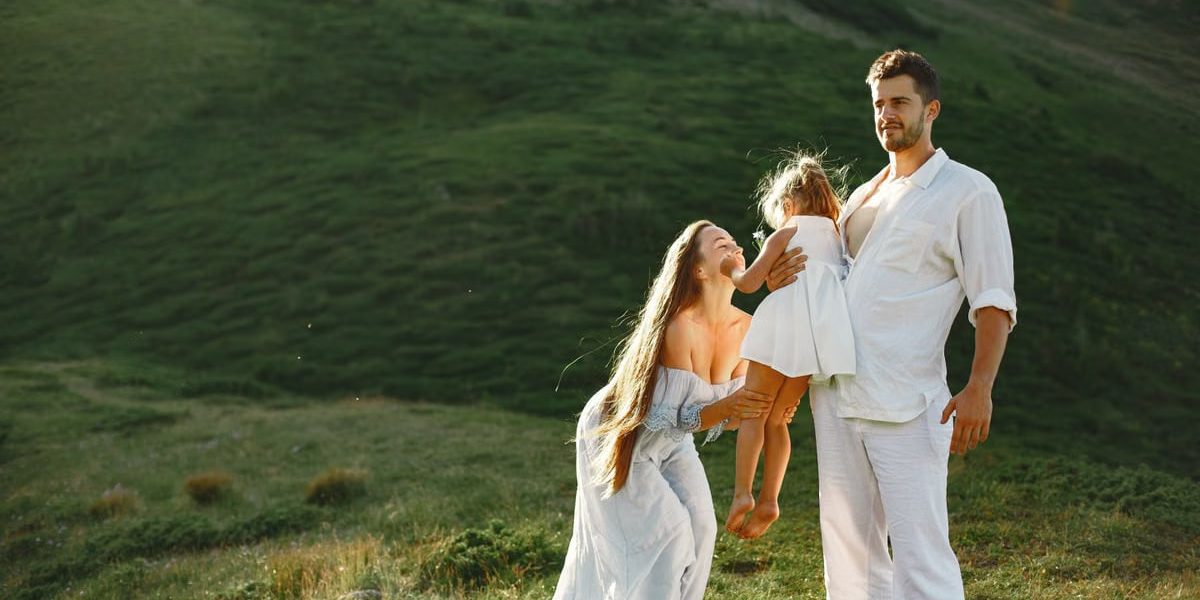 A joyful family of three in white clothing enjoying the outdoors on a sunny day.
