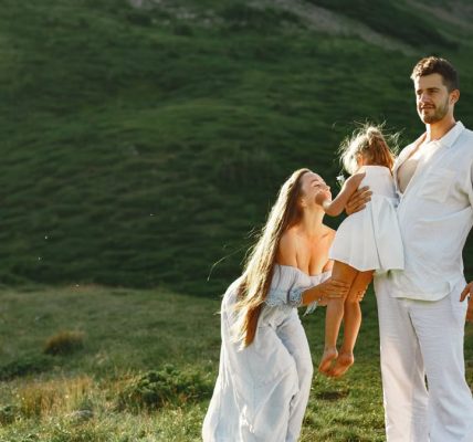 A joyful family of three in white clothing enjoying the outdoors on a sunny day.