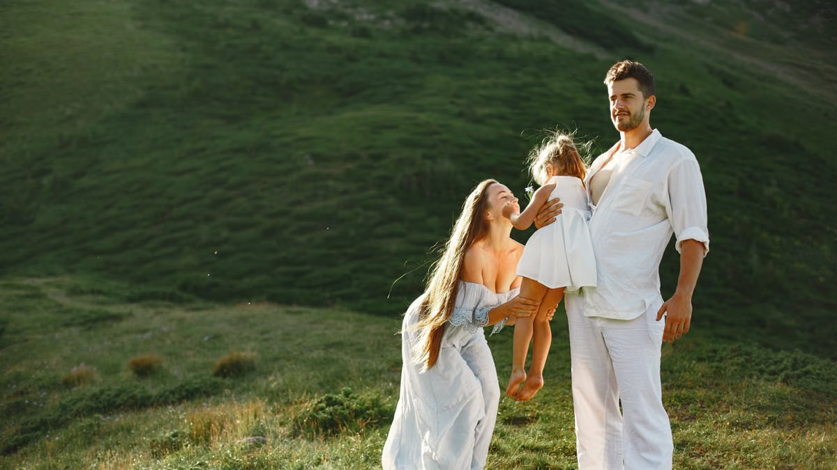 A joyful family of three in white clothing enjoying the outdoors on a sunny day.