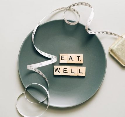 Flat lay of scrabble tiles spelling 'eat well' on a plate with a tape measure, promoting healthy eating.